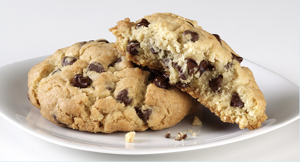 A chocolate chip cookie on a plate temptingly parted to showcase its gooey inside.