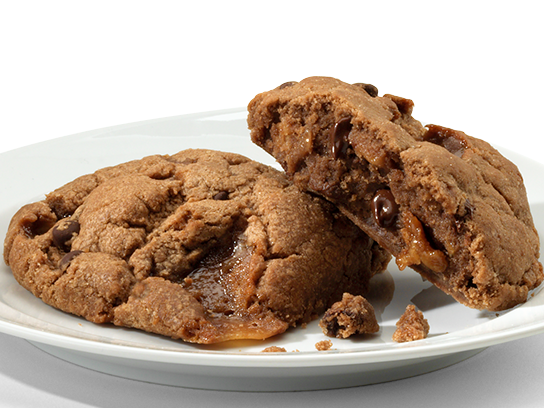 Two toffee fudge brownie cookies, one broken to reveal gooey inside, on a plate.